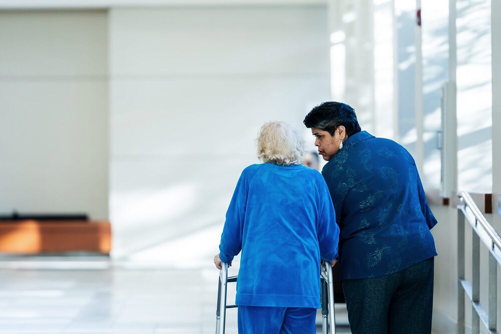 Soignante accompagnant une personne âgée dans un couloir d'établissement
